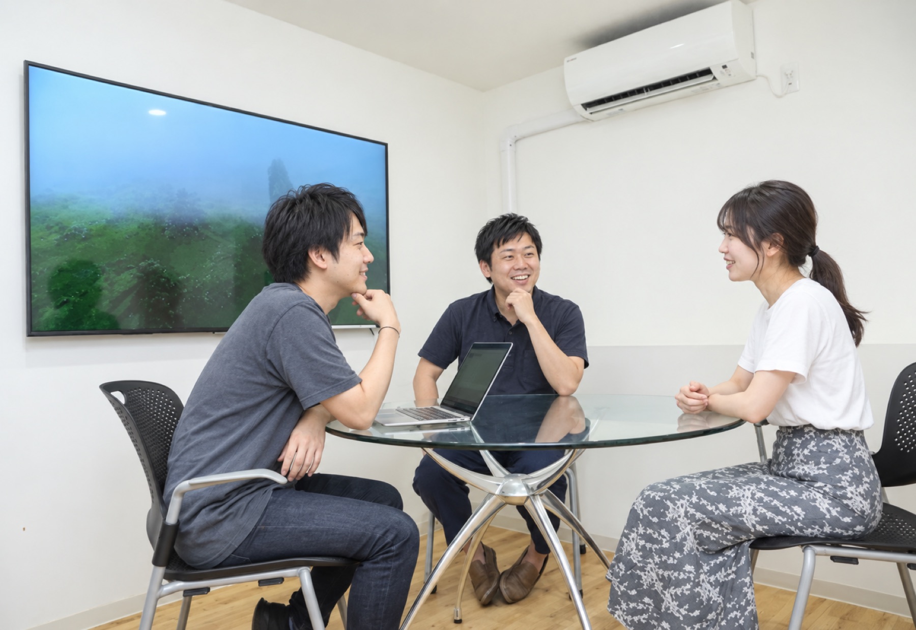 丸テーブルを囲み、自然に会話する三人のメンバーのイメージ