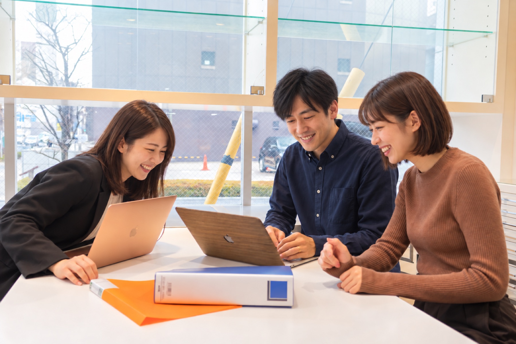 テーブルを囲み、パソコンを見ながら話すメンバーたち（AIで生成した架空の人物によるイメージ）